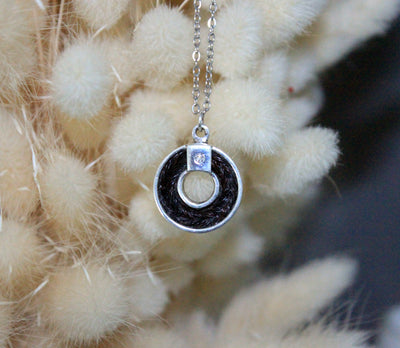 Sterling silver pendant holding braided horsehair with a sparkling diamond set on a natural soft white background