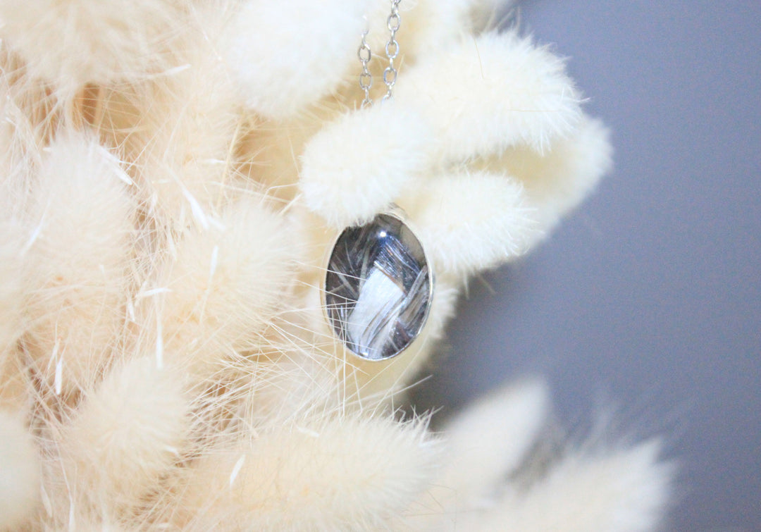 Close up of a glass oval pendant inlaid with braided multi colored horsehair against a soft background