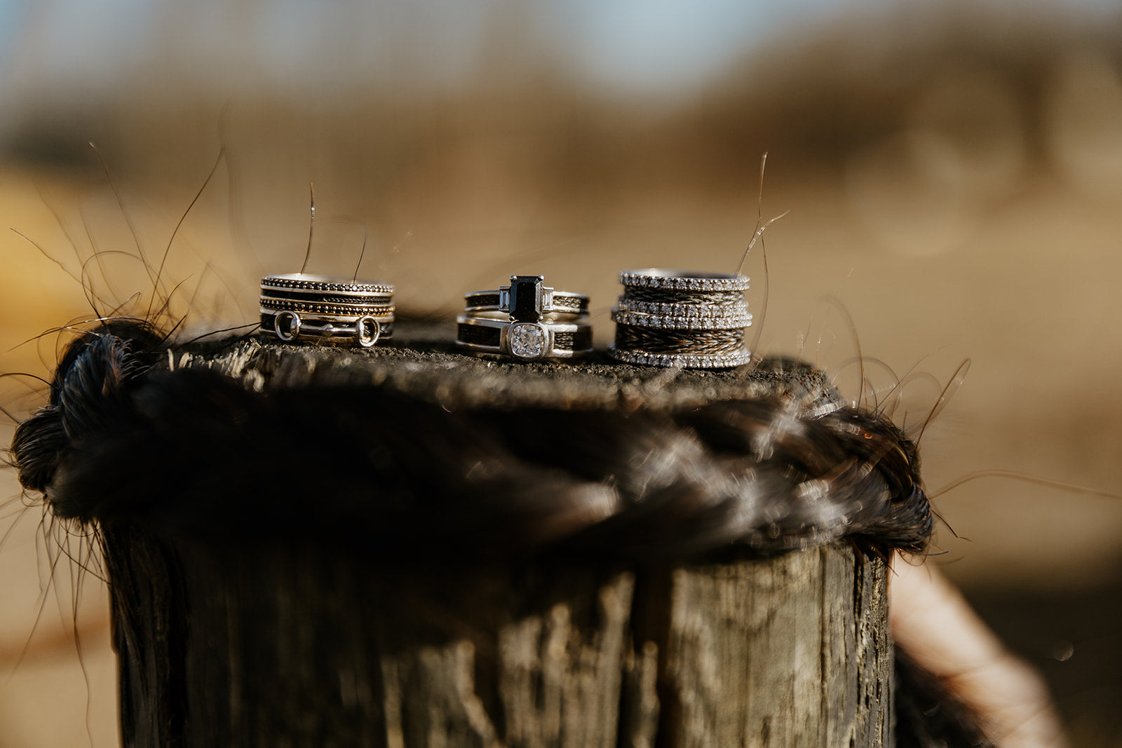 Horsehair rings in gold with diamonds stacked on top of eachother with a braided section of horse tail all sitting on a fence post