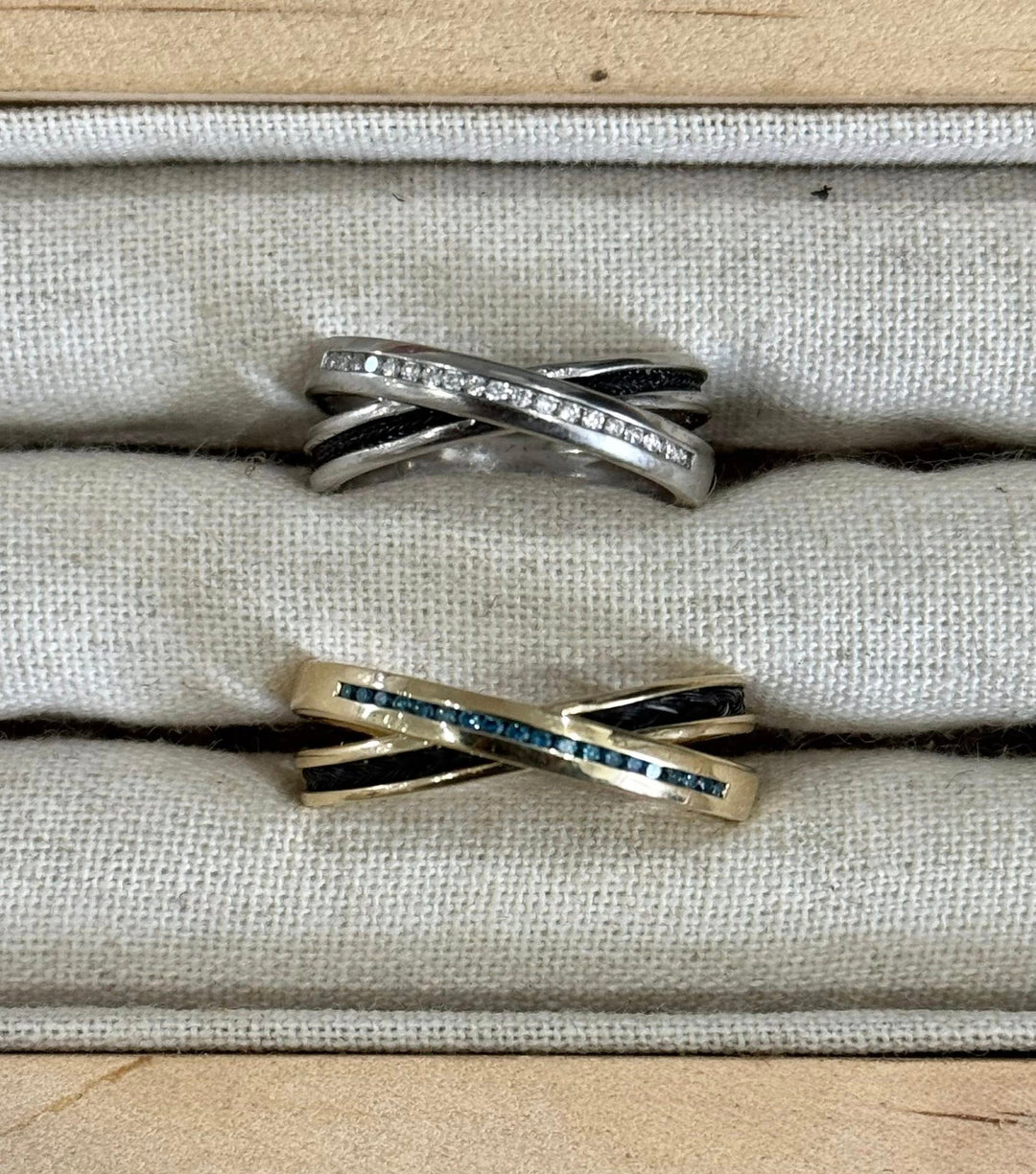 Two Cambridge horsehair rings, criss cross design. Shown in sterling silver with cz stones and yellow gold with blue diamonds. Horsehair set into rings