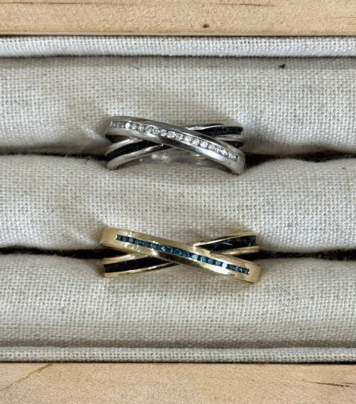 Two Cambridge horsehair rings, criss cross design. Shown in sterling silver with cz stones and yellow gold with blue diamonds. Horsehair set into rings