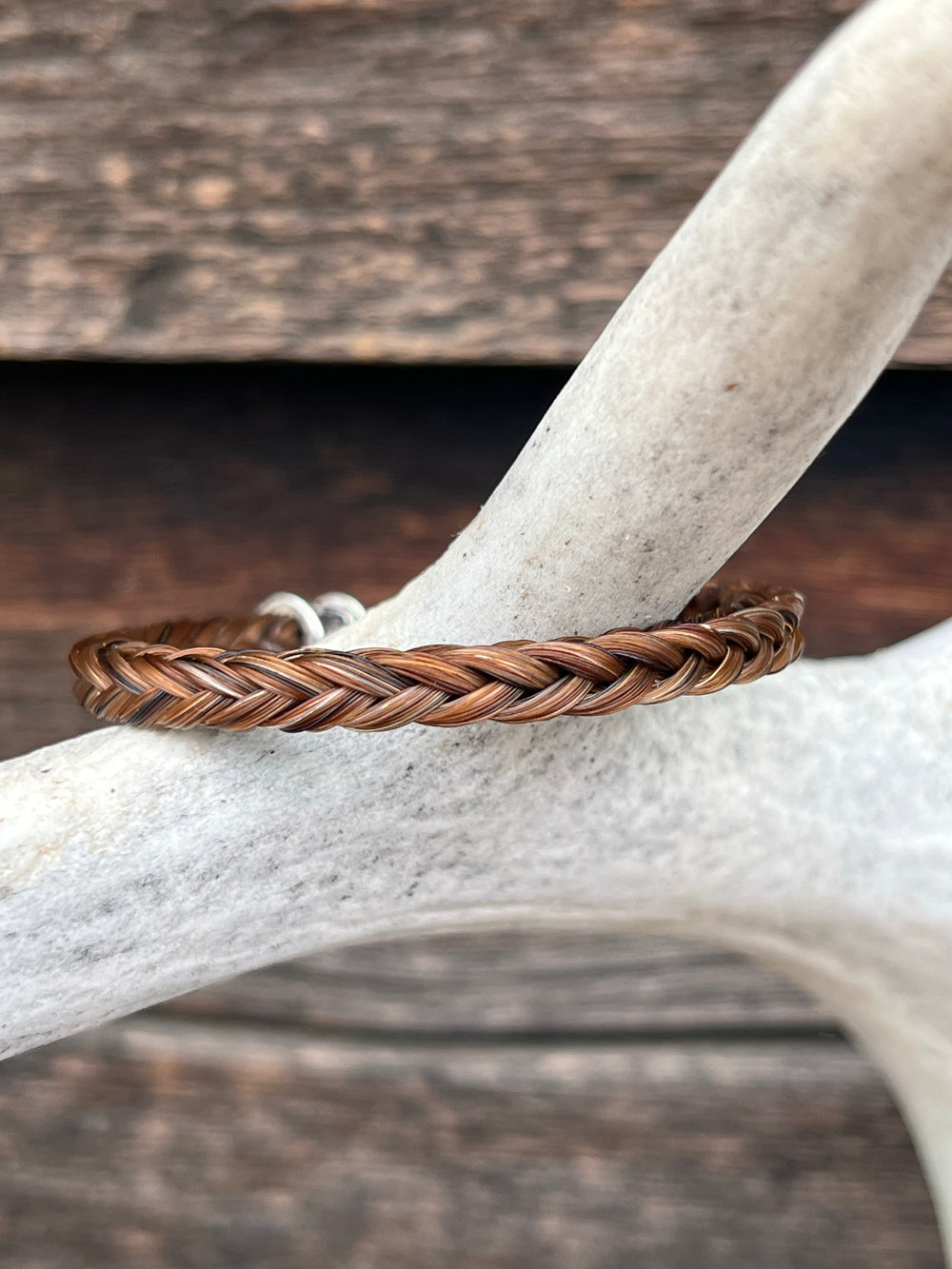 A braided horsehair bracelet with sterling silver ends, displayed on a deer antler against a wooden background.